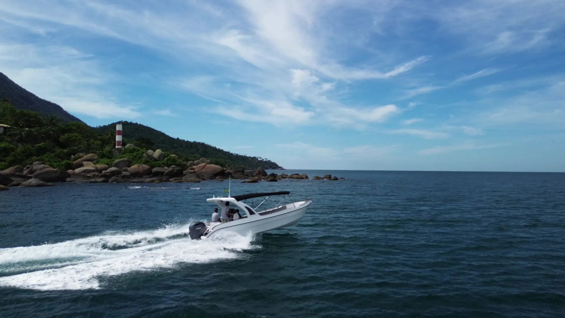 Lancha sobre o mar azul, com montanhas e vegetação ao fundo